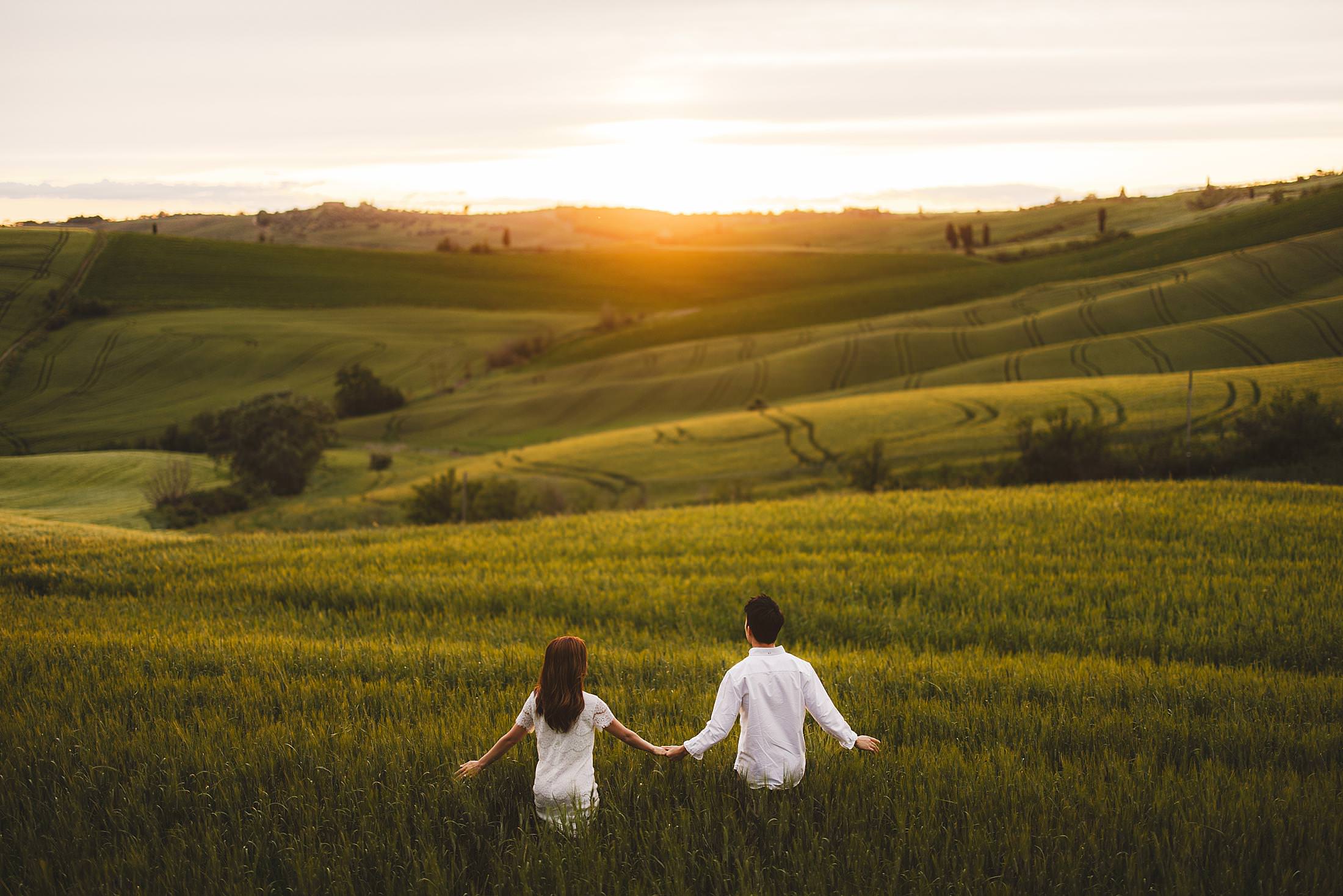 Romantic engagement photo session with warm hues of an unexpectedly golden sunset on a countryside field near Pienza